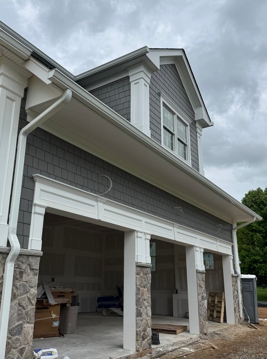Gray shake home garage wing with white columns on fieldstone piers and a shake dormer, built by North Valley Exteriors