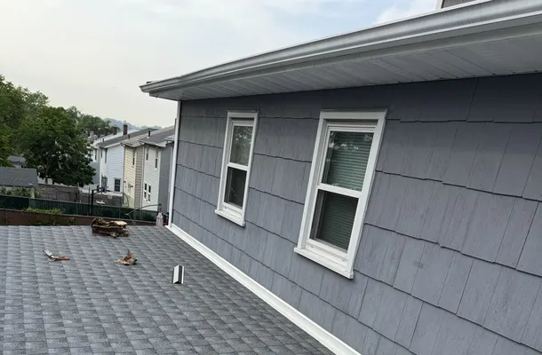 New architectural asphalt shingle roof meeting a clean gutter and gray shake siding by North Valley Exteriors
