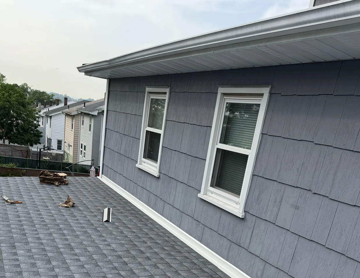 New architectural asphalt shingle roof meeting a clean gutter and gray shake siding by North Valley Exteriors