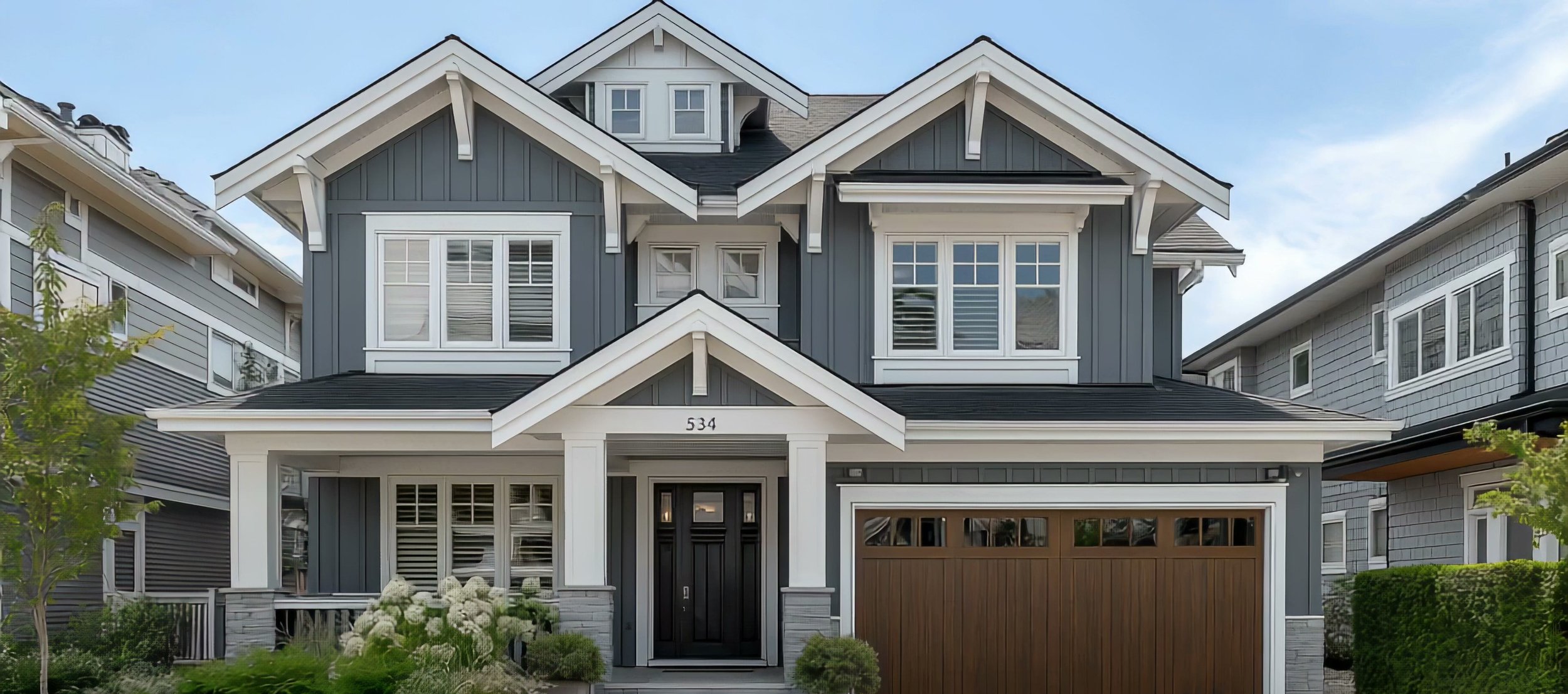 Finished dark-gray board-and-batten home with white trim, a gabled entry portico and a stone base by North Valley Exteriors