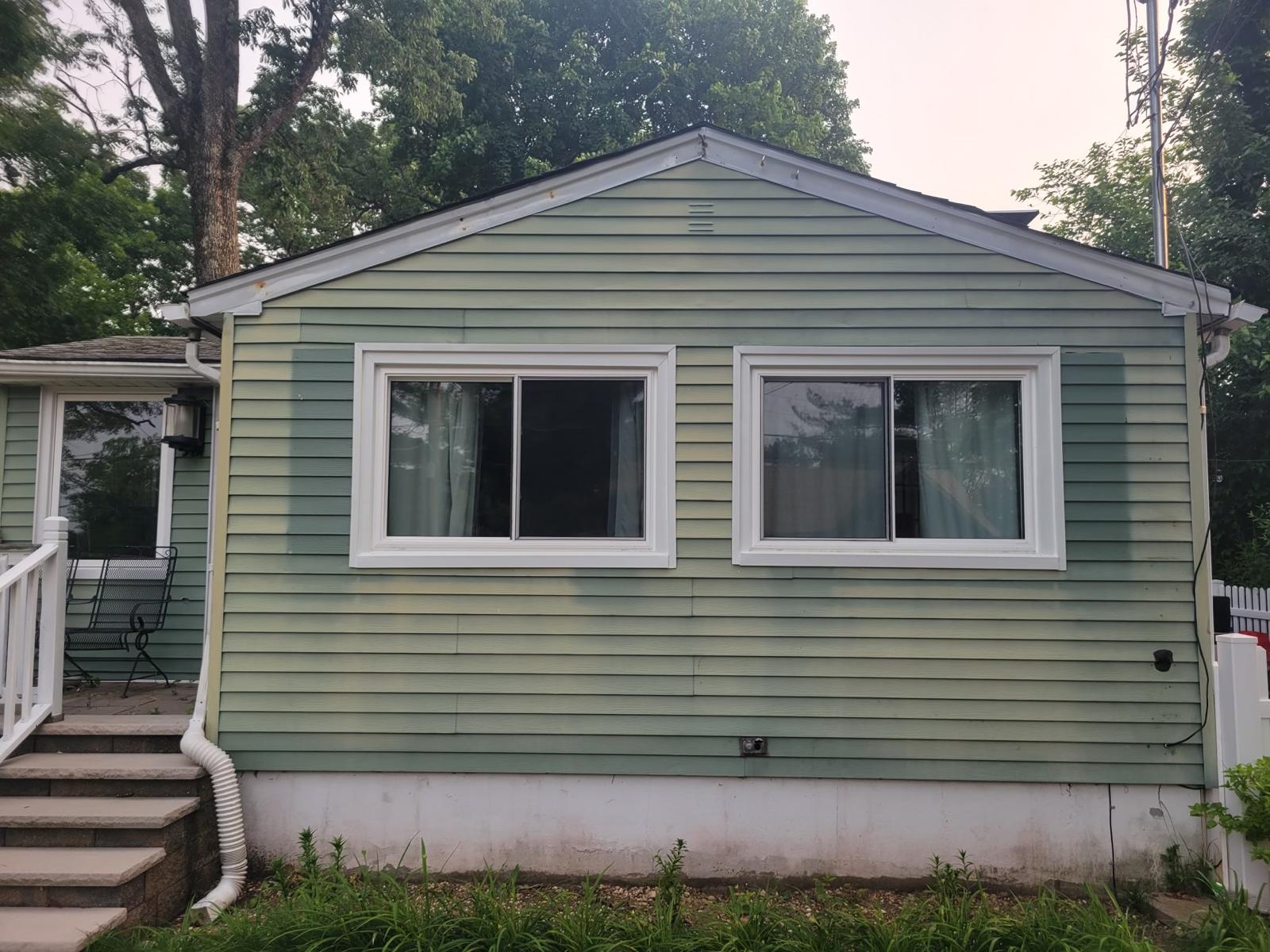 Before: the cottage in its original green vinyl lap siding, with white-trimmed windows on the gable end and the front steps at left