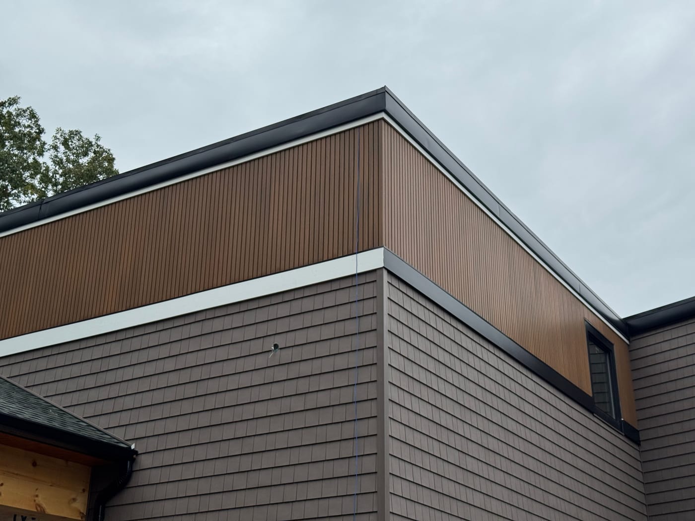 Corner detail of a wood-tone vertical accent band over brown shake siding