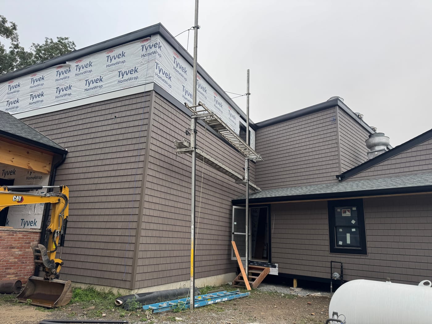 Brown shake siding going on with black coping and a covered work area