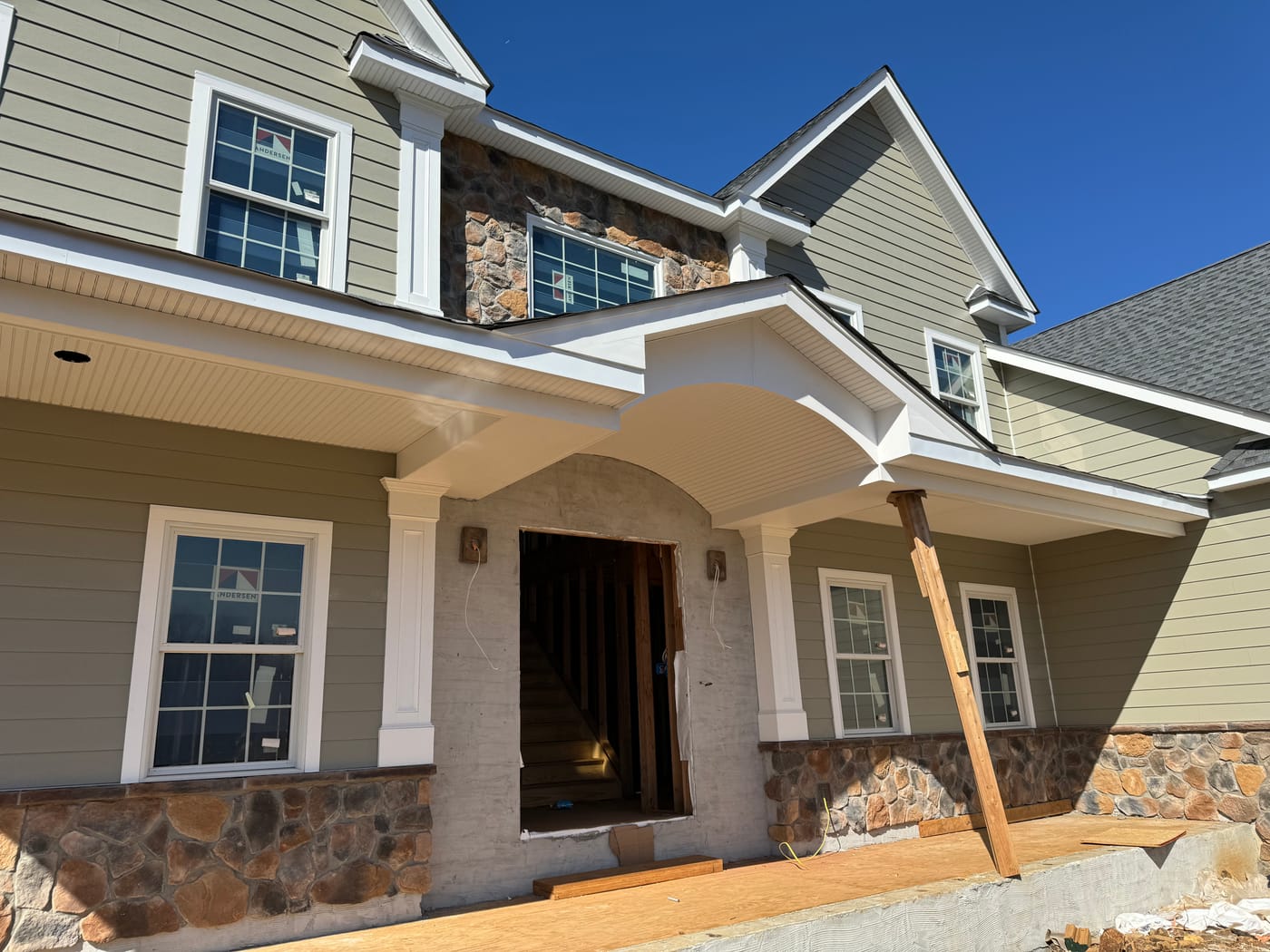 Finished sage lap entry with a curved beadboard portico and fieldstone wainscot