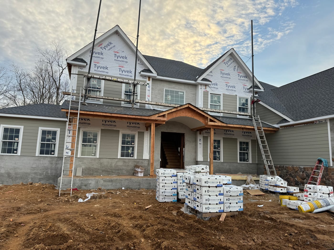 Tan lap two-story with the timber arched porch framed and stone pallets staged