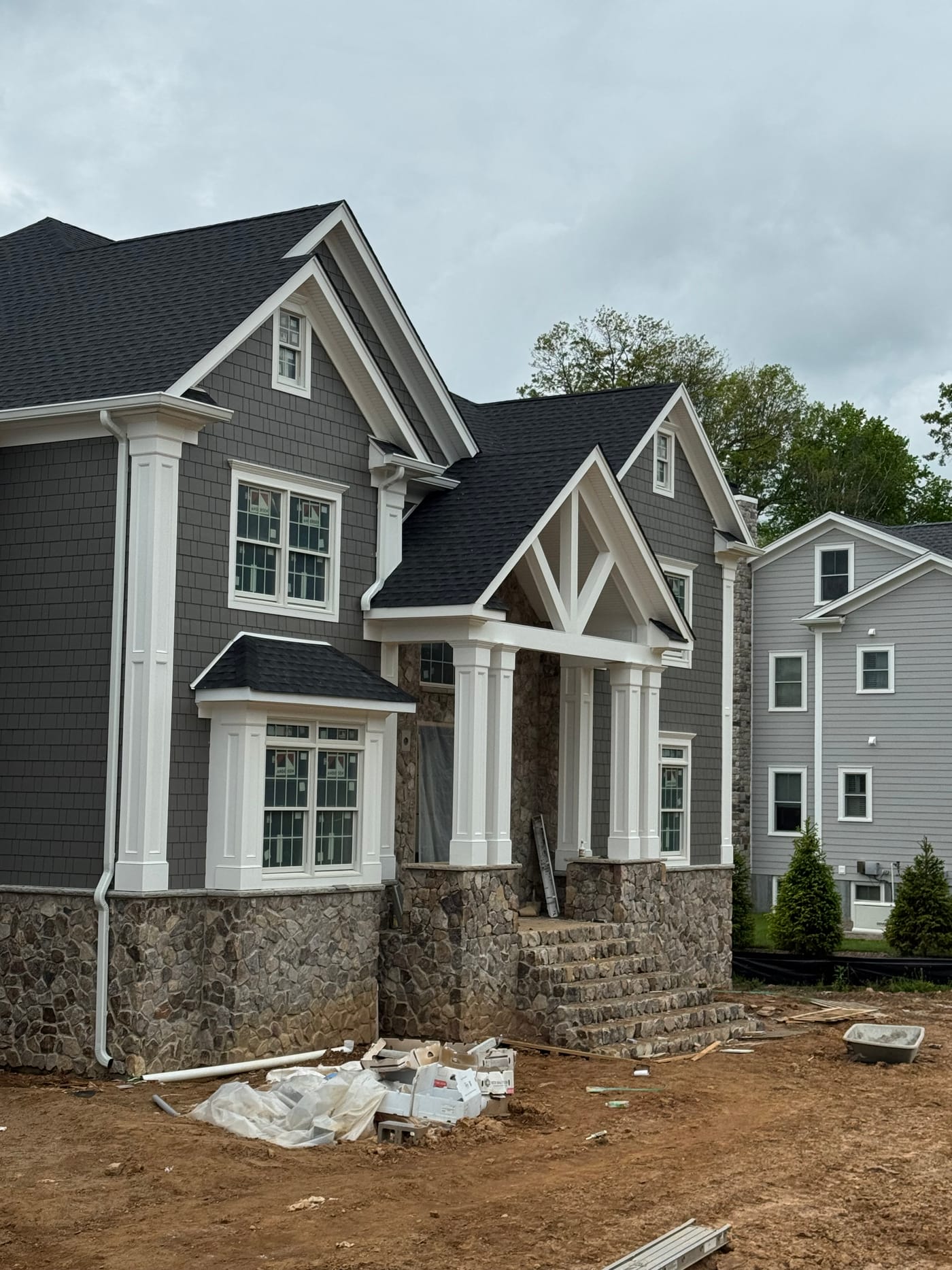 Finished dark-gray shake home with a wraparound porch and columns on stone piers