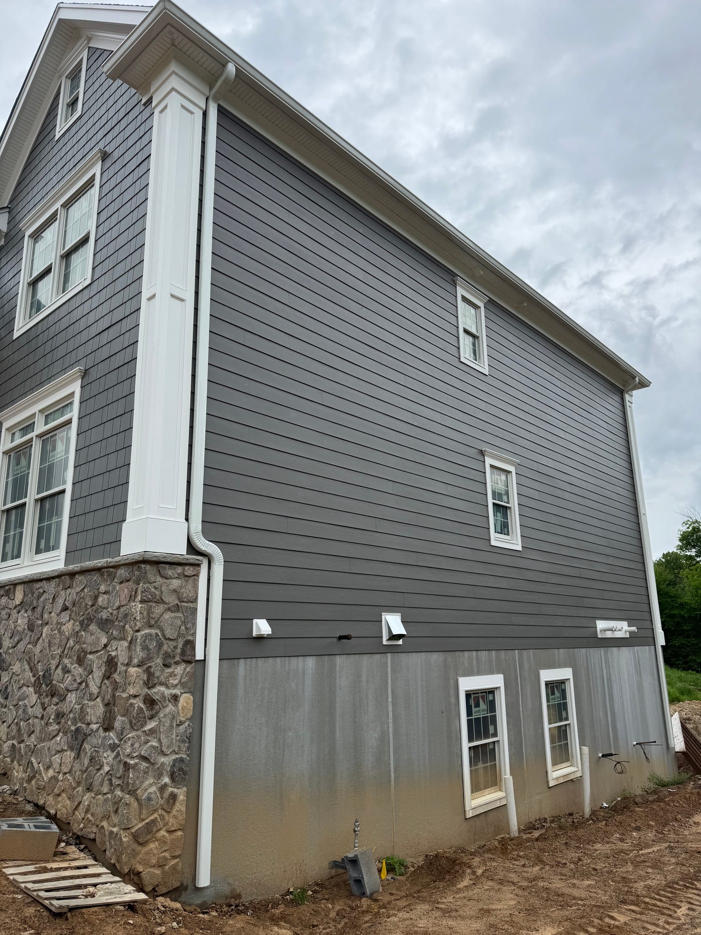 Large gable end in gray vertical board and lap siding over a fieldstone water table