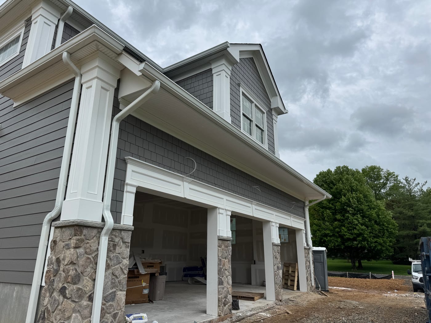 Garage wing with white columns on fieldstone piers and a shake dormer