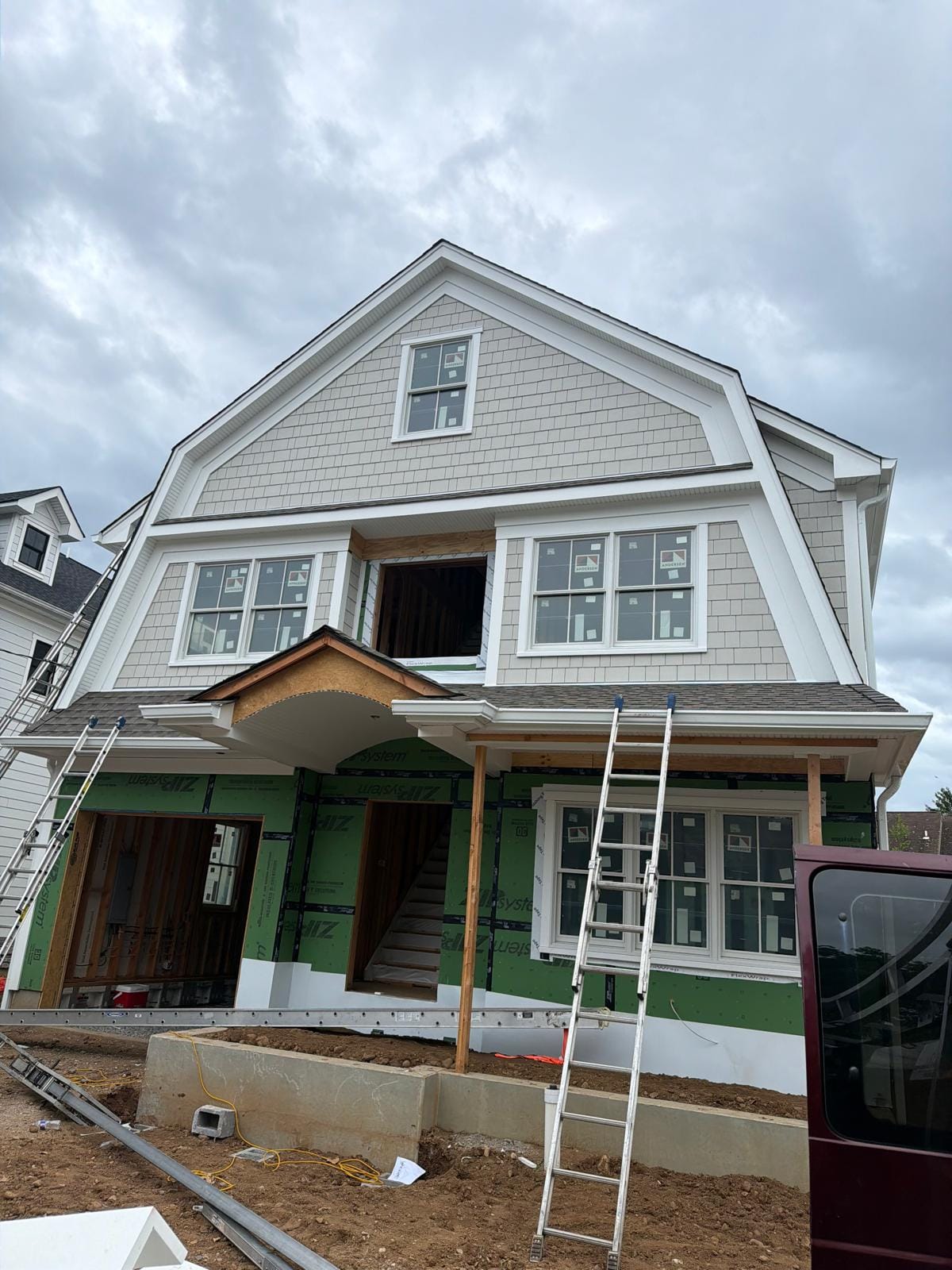 Gambrel home mid-build with ZIP System sheathing and a raw curved portico