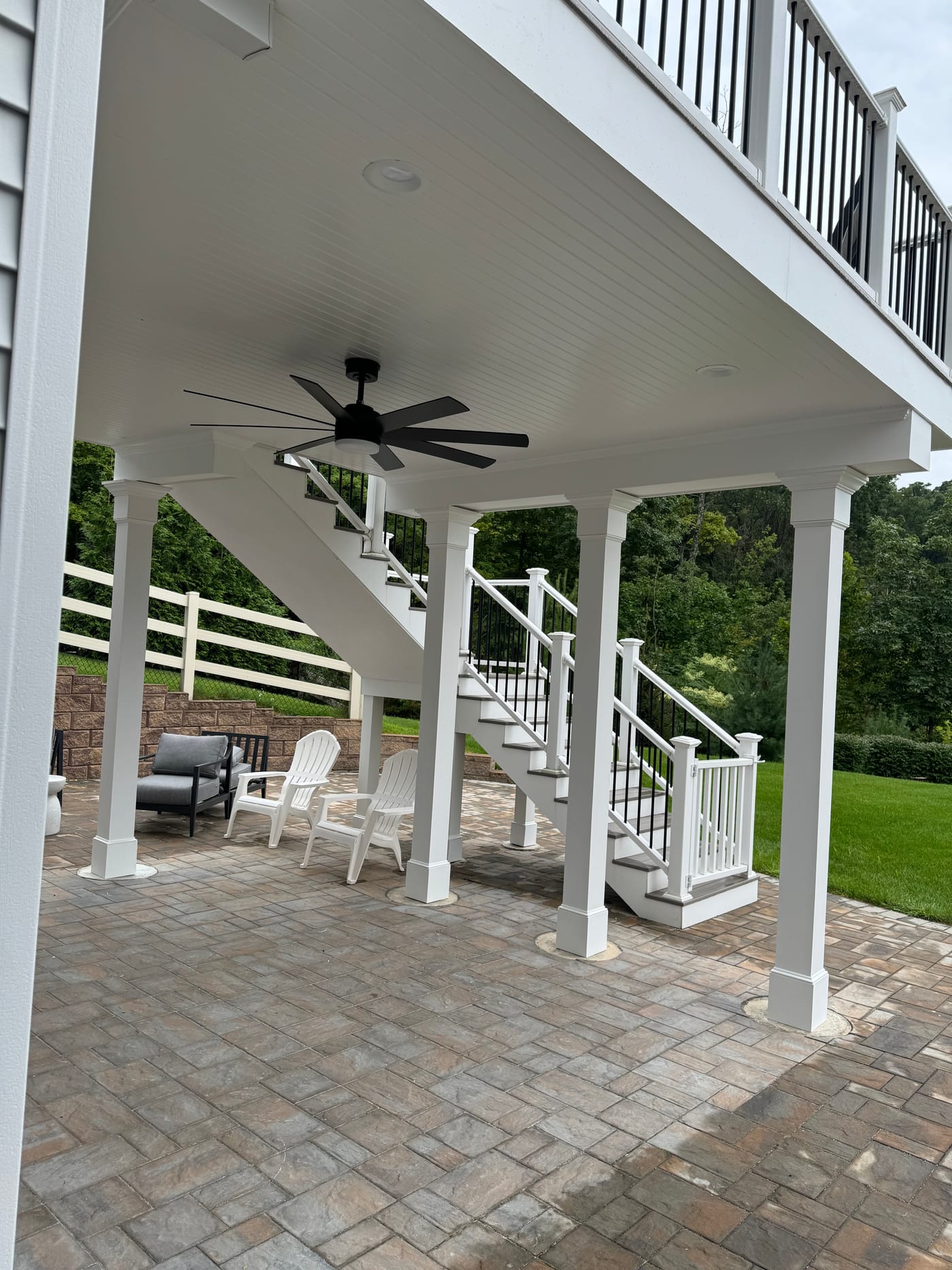 Under-deck patio with a black ceiling fan and the composite deck above
