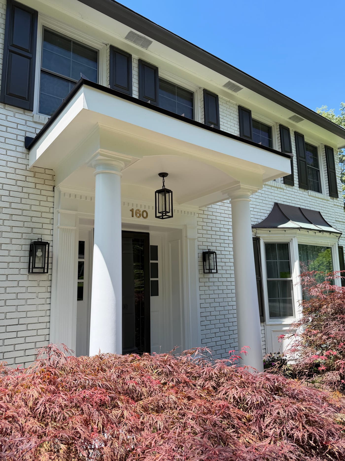 White brick colonial with a scrolled entry portico and black-framed windows