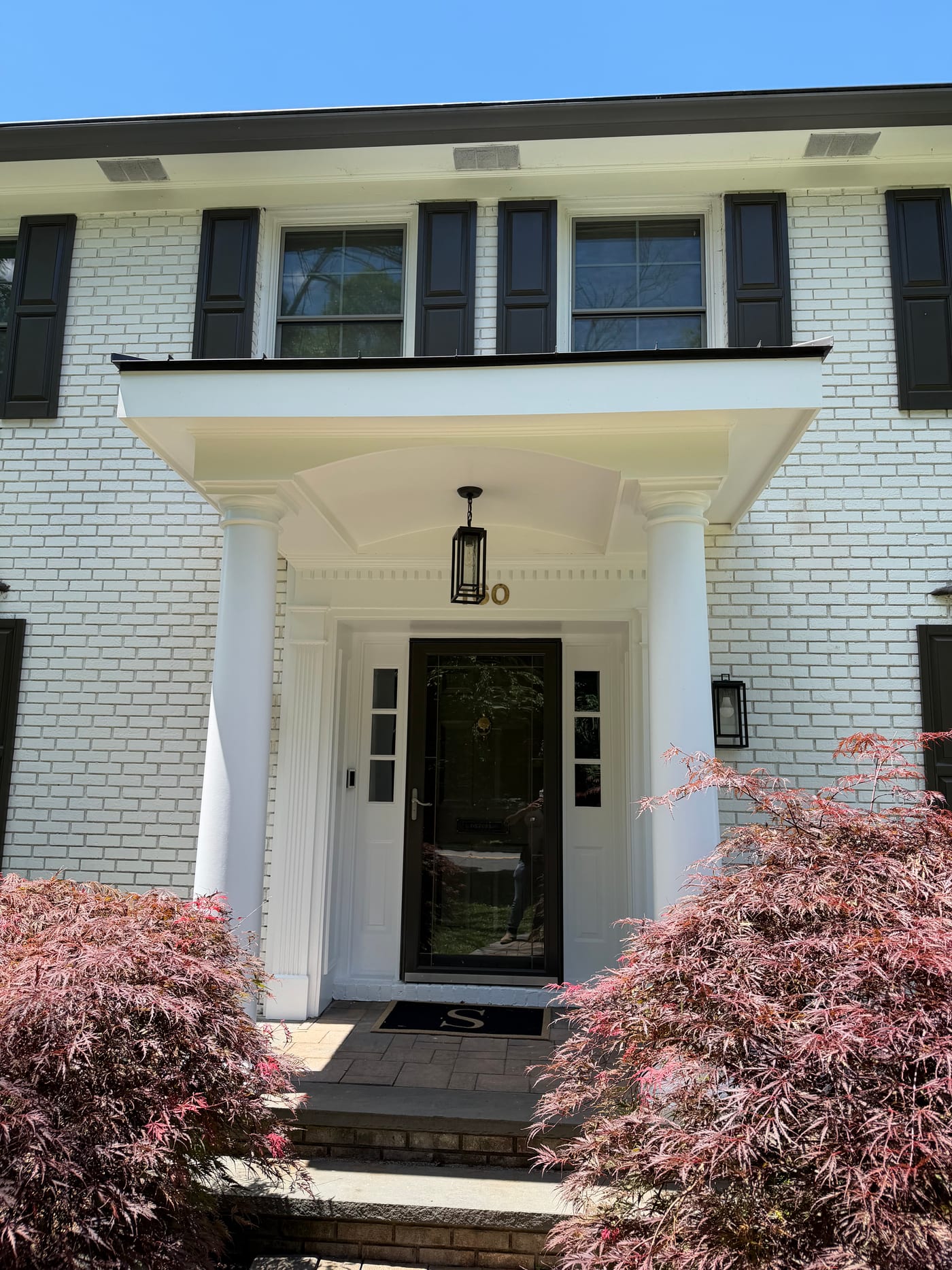 Straight-on view of the white scroll portico on fluted columns over painted white brick