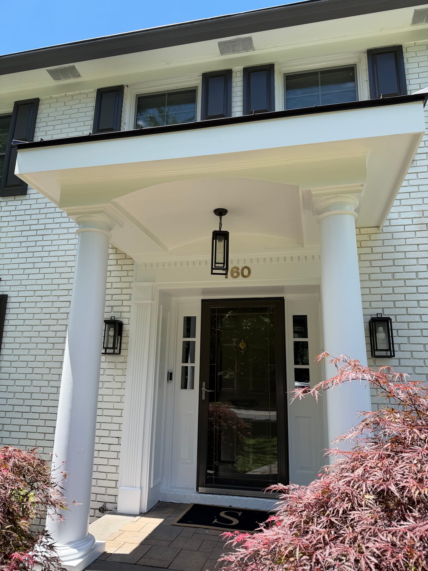 Scroll portico entry with carriage lanterns and a black front door