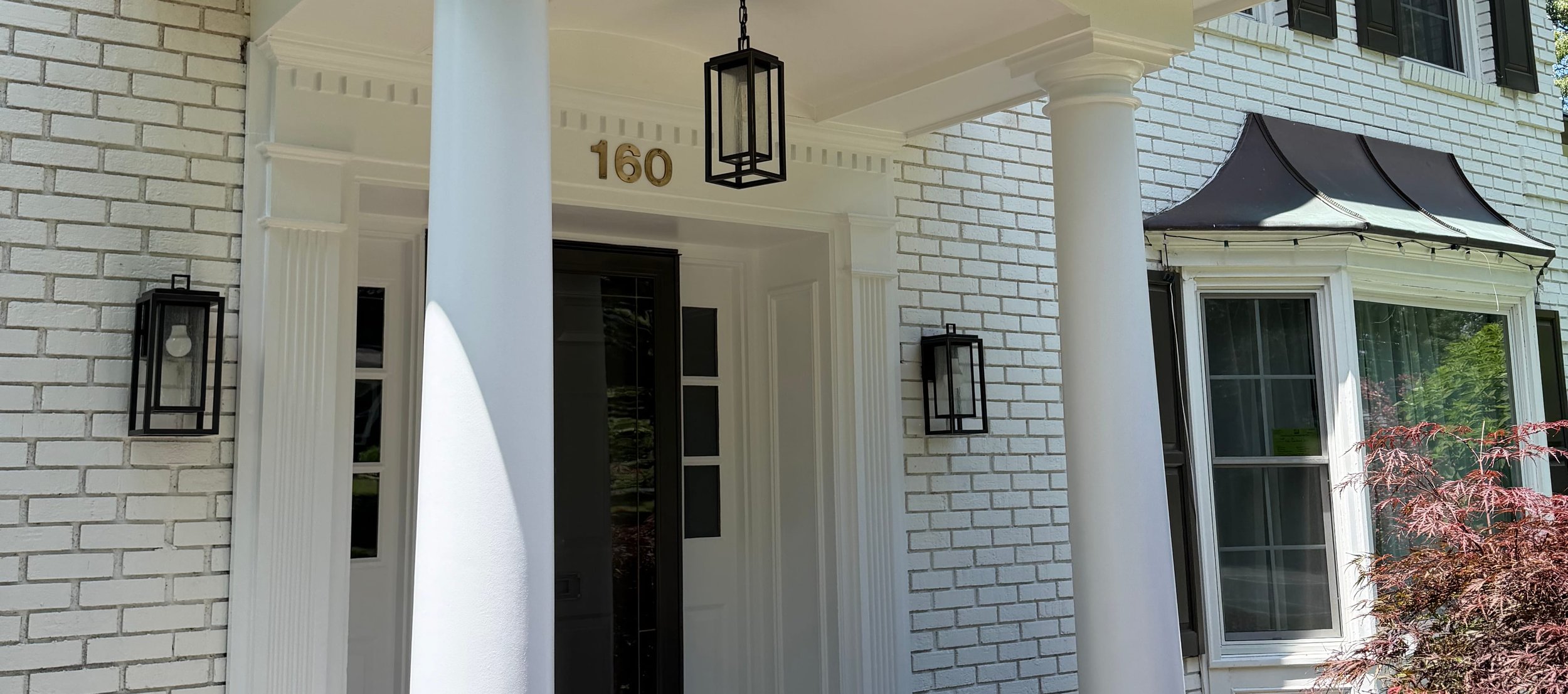 White scrolled entry portico on fluted columns with black carriage lanterns over painted white brick, built by North Valley Exteriors